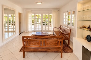 A room with a wooden bench, a glass shelf with decorative items, and a view through large glass doors. - New Listing (Arraial d'Ajuda)