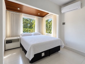 A modern bedroom with a large bed, a nightstand, an air conditioning unit, and a view of greenery outside. - New Listing (Arraial d'Ajuda)