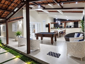 A spacious indoor area with a pool table, wicker furniture, and a kitchen in the background. - New Listing (Arraial d'Ajuda)