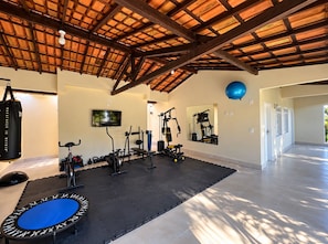 A spacious gym with various exercise equipment, a large mirror, and a ceiling with wooden beams. - New Listing (Arraial d'Ajuda)