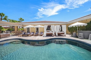 A swimming pool with lounge chairs and umbrellas, surrounded by a covered patio area. - All-Inclusive Retreat: Pool | HotTub | Golf | Games (Indio)