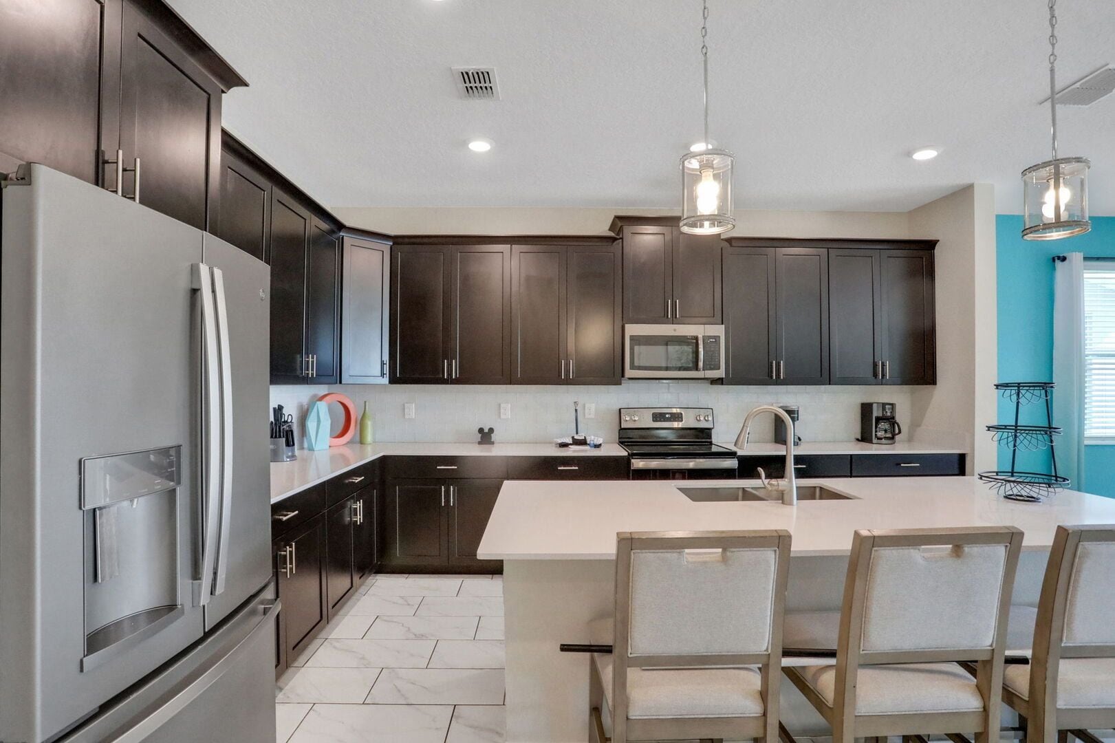 Una cocina moderna con armarios oscuros, electrodomésticos de acero inoxidable, una isla central con asientos e iluminación colgante.