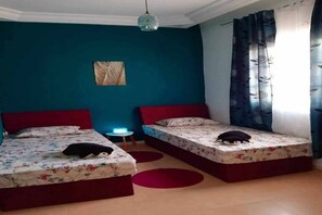 A bedroom with two beds, a nightstand, a wall-mounted lamp, and a window with curtains. - Apartment "NAFAS"❤️ de la résidence Maisons Maktoub Djerba ❤️ (Djerba)