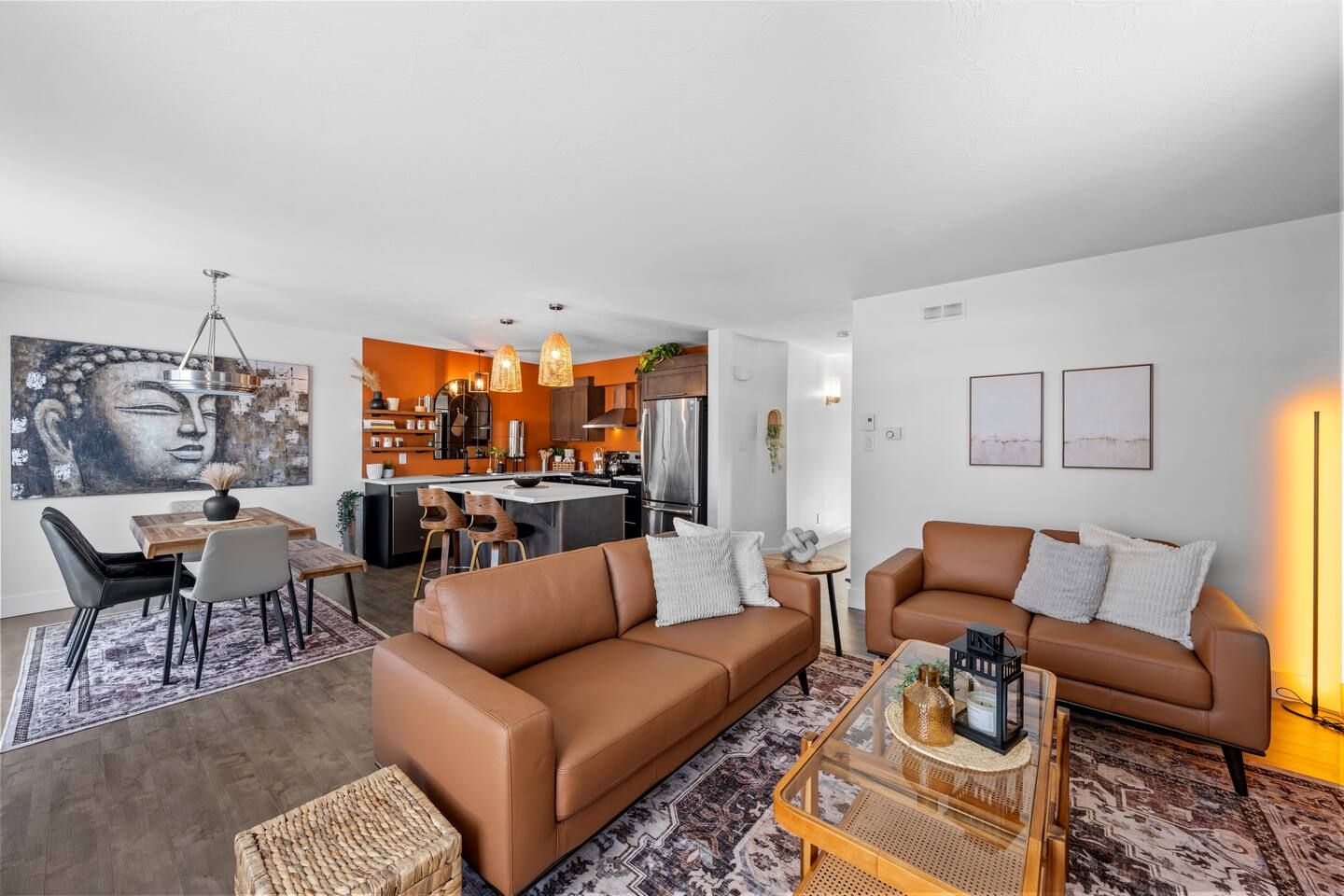 A modern living room with a brown sofa, a dining area with a table and chairs, and a kitchen in the background.