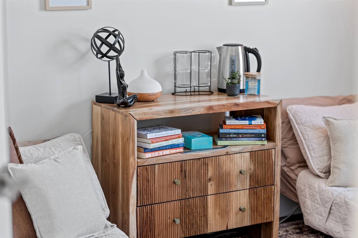 Una libreria in legno con libri e oggetti decorativi, un vaso bianco e una scultura in metallo.