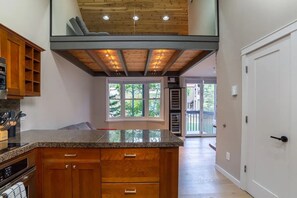 A kitchen with a granite countertop, wooden cabinets, and a view through a window to the outdoors. - Ski-in ski-out condo with mountain views, balcony, wifi, full kitchen. (Mountain Village)