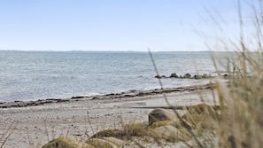Ein Strand mit felsigem Ufer, ruhigem Wasser und weiter Küstenlandschaft im Hintergrund.