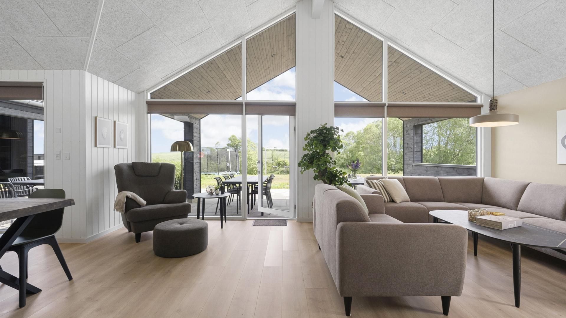 A spacious living area with a high ceiling, a dining table, a sofa, and a large window providing a view of the outdoors.