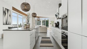 A modern kitchen with a central island, white cabinetry, and a view to the outdoors. - VillaVilla 1022 - Ebeltoft, Østjylland (Ebeltoft)