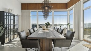 Een eetruimte met een lange houten tafel, zwarte stoelen en een moderne kroonluchter.