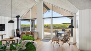 A spacious living area with a fireplace, comfortable seating, and large windows offering a view of the outdoors. - VillaVilla 1015 - Hvide Sande, Vestjylland (Hvide Sande)
