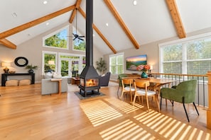 A spacious living area with a high ceiling, wooden beams, a fireplace, and a dining area with chairs and a table. - Woodland Lodge - 20 Acres - Sleeps 10 (Taylors)
