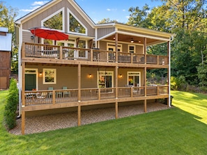 A two-story wooden house with a balcony, outdoor seating, and a red umbrella. - Woodland Lodge - 20 Acres - Sleeps 10 (Taylors)