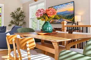 A dining area with a wooden table, chairs, a vase with flowers, and a painting on the wall. - Woodland Lodge - 20 Acres - Sleeps 10 (Taylors)