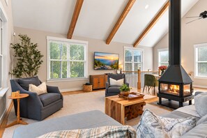 Un salon chaleureux avec une cheminée, des fauteuils confortables et de grandes fenêtres.