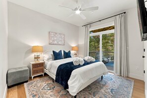 A bedroom with a bed, nightstands, a window with curtains, a ceiling fan, and a view of the outdoors. - The Lodge at Woodland Acres (Taylors)