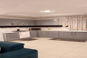 A modern kitchen with grey cabinets, a white countertop, and a blue sofa in the foreground. - Apartment " Eshq " de la résidence Maisons Maktoub Djerba❤️ (Djerba)