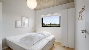 A minimalist bedroom with a bed, a window with a view, and a wardrobe. - VillaVilla 1023 - Hasmark Strand, Fyn og øer (Otterup)