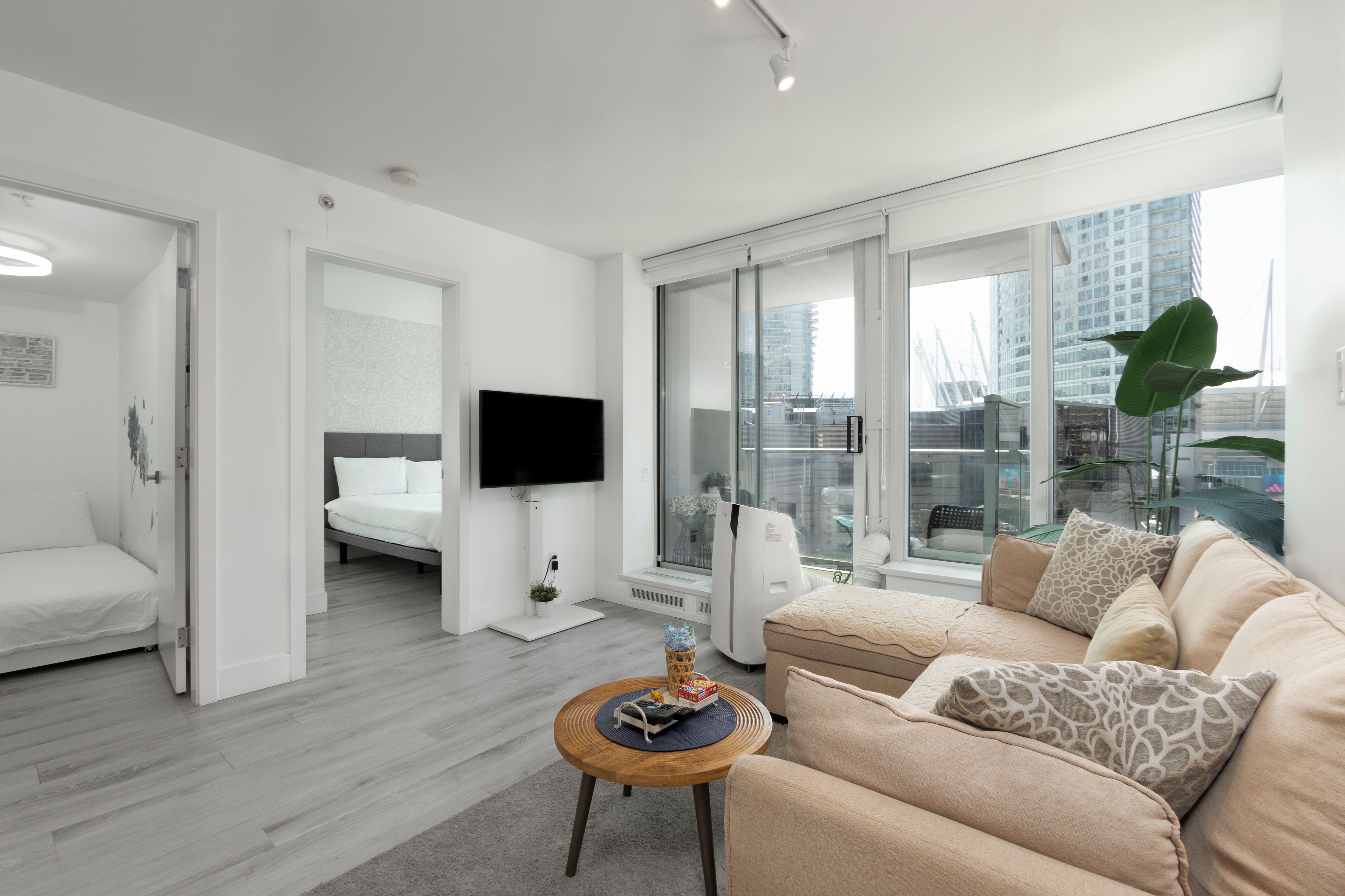 Un salon moderne avec un canapé, un téléviseur et une vue sur la ville grâce à de grandes fenêtres.