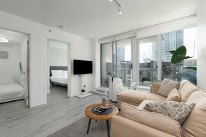 Sala de estar moderna com sofá, TV e vista da cidade através de grandes janelas.