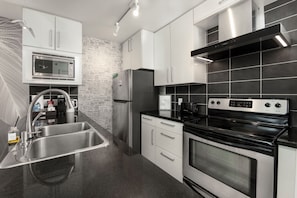A modern kitchen with stainless steel appliances, a black tiled backsplash, and a sleek design. - Downtown Vancouver 1BR + Den -  Parking - 90+ Days (Vancouver)