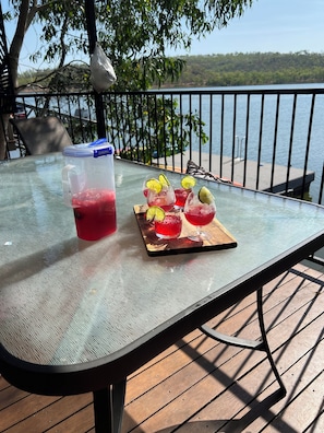 Ein Tisch mit einem Getränkespender und Gläsern, ein Holftablett mit Getränken und Blick auf einen See und Bäume.