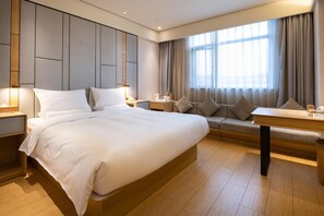 Een moderne hotelkamer met een groot bed, een bank, een bureau en een raam met gordijnen.