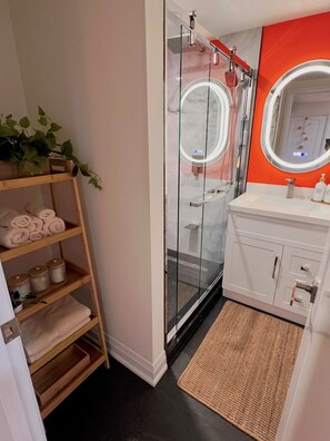 A bathroom with a glass shower enclosure, a white vanity with a mirror, and a wooden shelf with towels. - Private Toronto Suite | Free Parking • Near Airport & Downtown (Toronto)