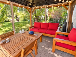 An outdoor patio with a wooden table, red sofa, and string lights. - Private Toronto Suite | Free Parking • Near Airport & Downtown (Toronto)