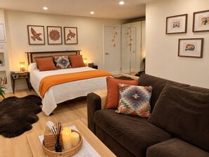 A well-lit bedroom with a bed, a brown sofa, a small table with candles, and framed artwork on the walls. - Private Toronto Suite | Free Parking • Near Airport & Downtown (Toronto)