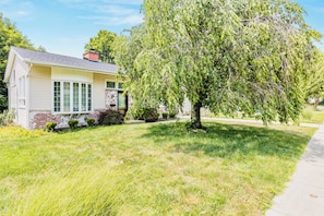 Ein eingeschossiges Haus mit Veranda, einem kleinen Garten und einem großen Baum davor.