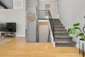 Ein modernes Wohnzimmer mit einem Flachbildfernseher, einer Treppe mit dekorativer Geländer und einer Topfpflanze.