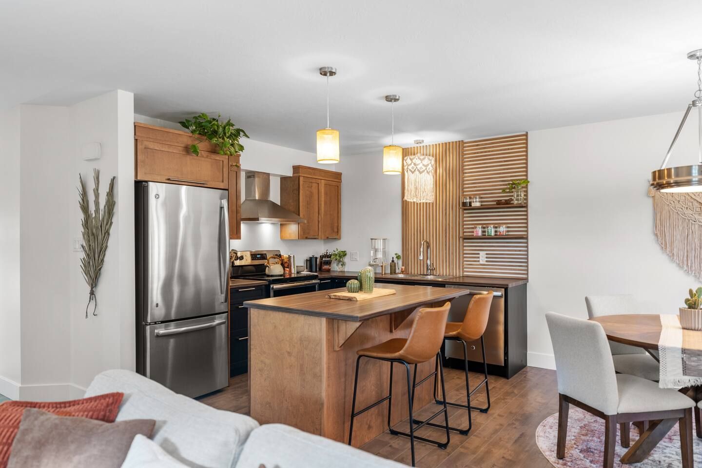 A modern kitchen with a stainless steel refrigerator, wooden cabinets, and a central island with bar stools.