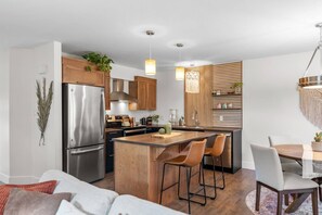 A modern kitchen with a stainless steel refrigerator, wooden cabinets, and a central island with bar stools. - Serenity City Retreat•Shine & Rise Wellness (Moncton)