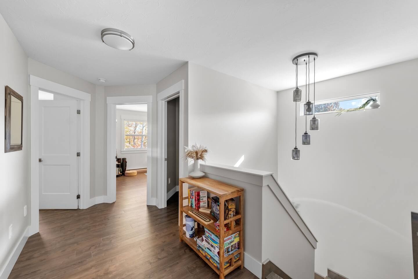 A hallway with a wooden bookshelf, white walls, and a staircase with a light fixture.