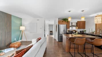 A modern kitchen with a central island, bar stools, and a dining area with a sofa.