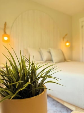 A bedroom with a bed, pillows, a potted plant, and wall-mounted lights. - Radiance City Retreat•Shine & Rise Wellness (Moncton)