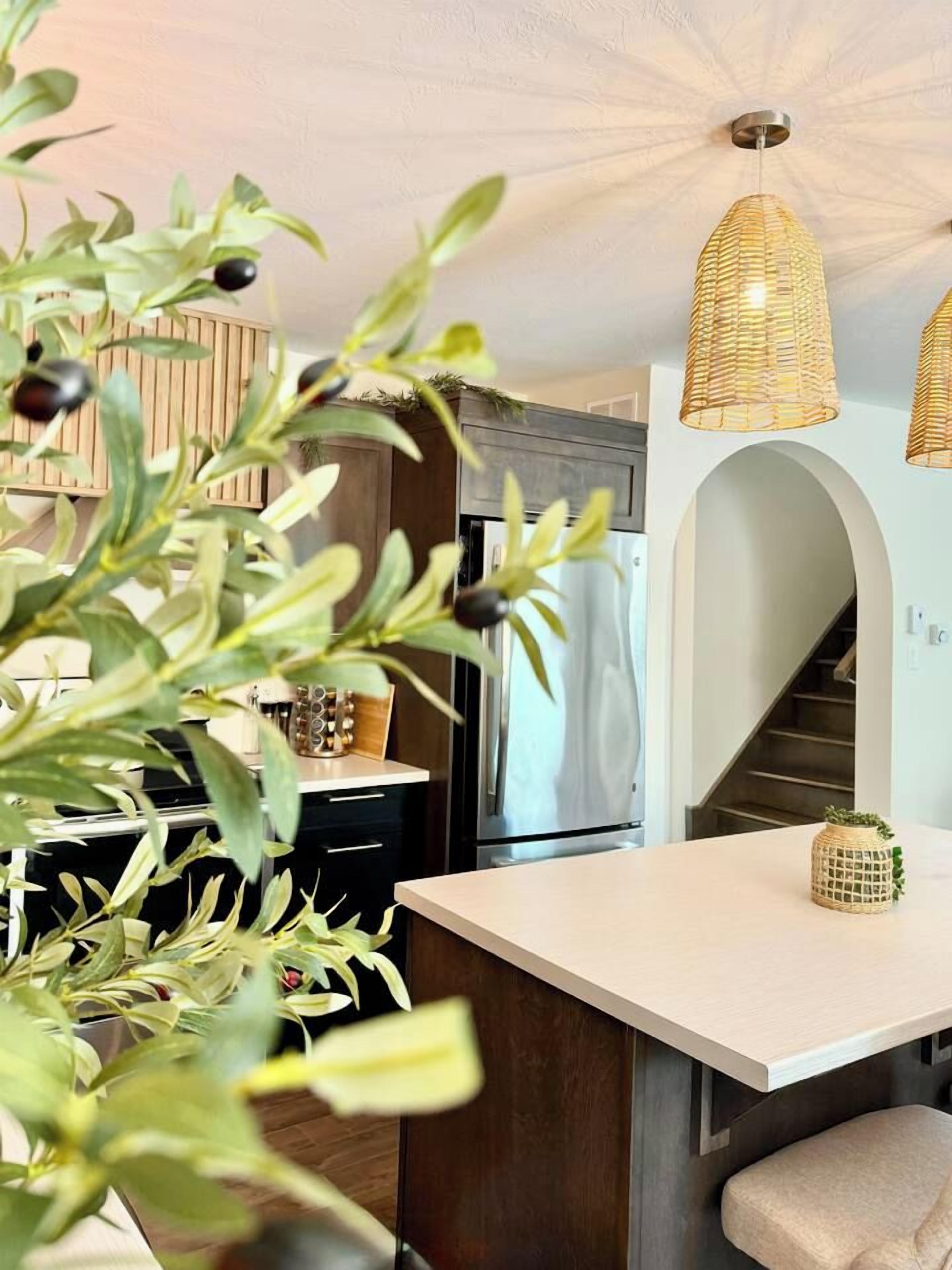A modern kitchen with a central island, overhead wicker pendant lights, and a staircase leading to an upper level.