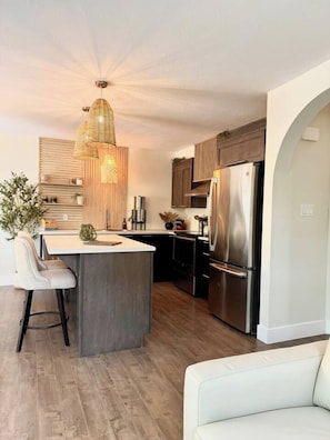 A modern kitchen with a central island, stainless steel appliances, and a hanging light fixture. - Radiance City Retreat•Shine & Rise Wellness (Moncton)