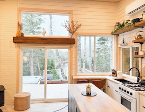 A modern kitchen with a large window, wooden cabinetry, and a built-in stove. - Eagle’s Nest Nature Retreat•Shine & Rise Wellness (Saint Mary Parish)