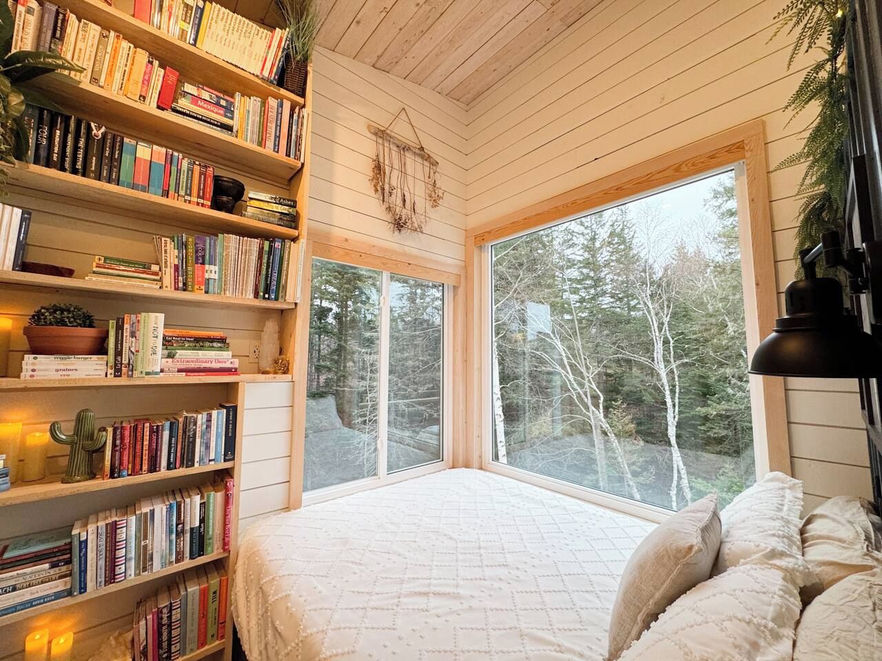 A cozy room with a large window, a bookshelf filled with books, and a bed with pillows.