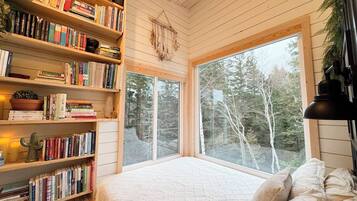 A cozy room with a large window, a bookshelf filled with books, and a bed with pillows.