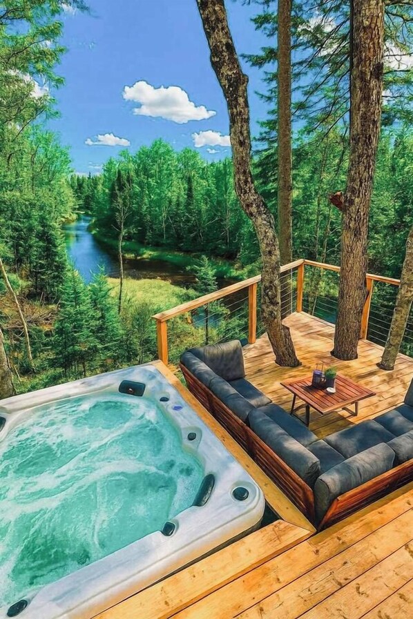A hot tub on a wooden deck with a view of a river and forest.