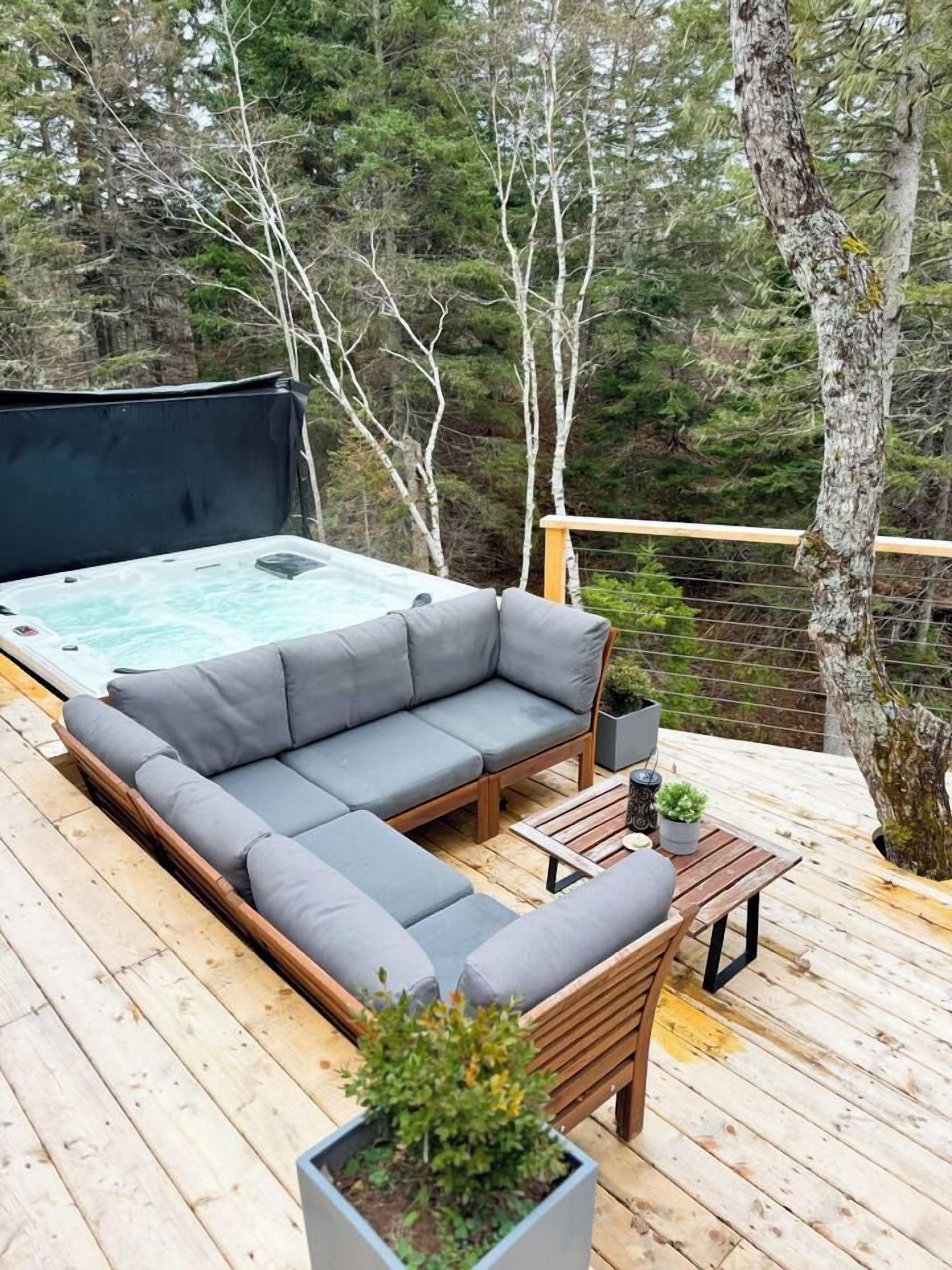 A wooden deck with a sectional sofa, a small table, and a hot tub.