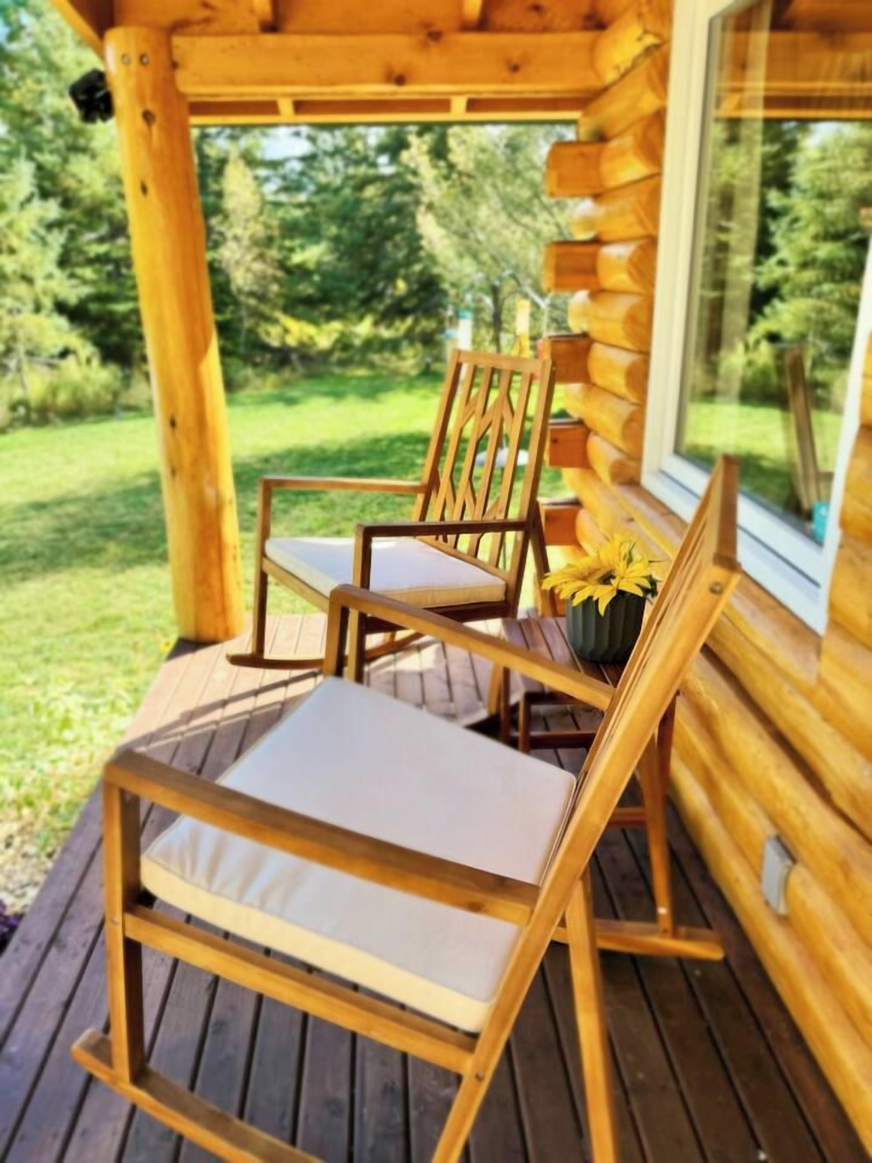 A wooden deck with two chairs and a table, a window, and a view of greenery.