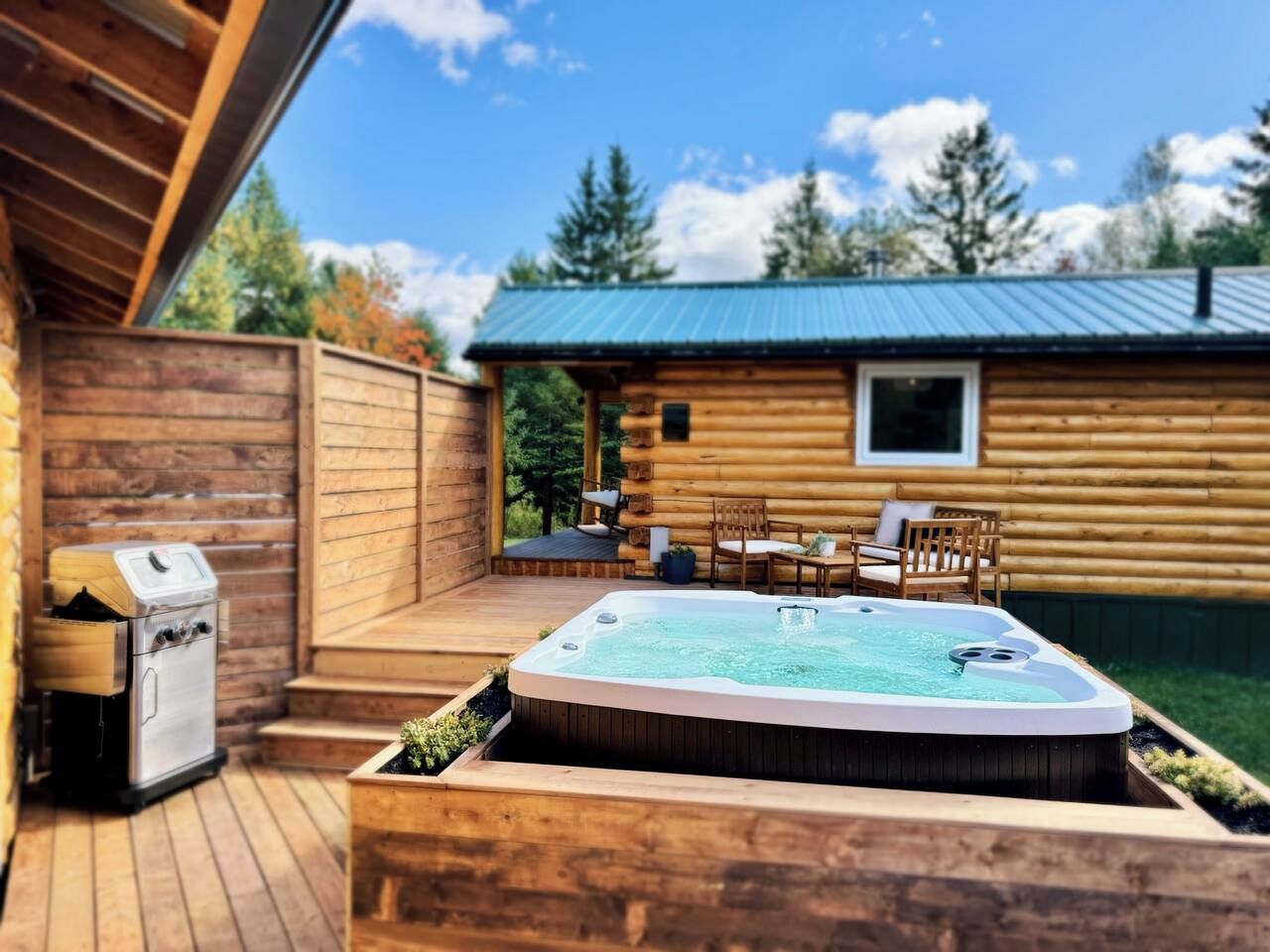 Una cabana de fusta amb un banyera d'hidromassatge, espai exterior per seure i una barbacoa.