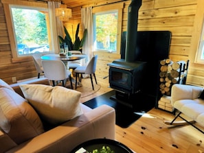 A cozy cabin interior with a sofa, chairs, a dining table, and a wood-burning stove. - Harmony Nature Retreat•Shine & Rise Wellness (Saint Mary Parish)