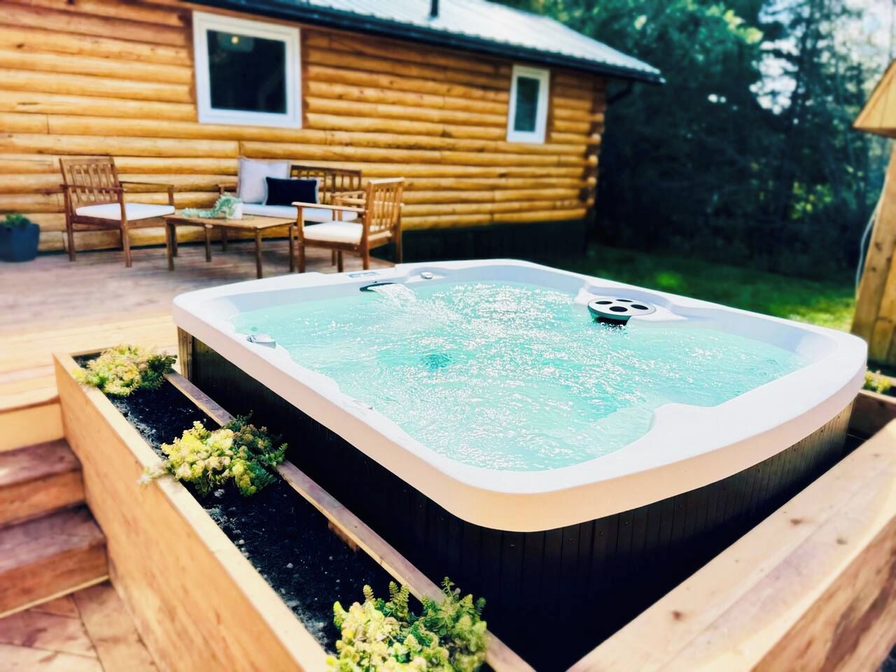 A hot tub in a wooden planter with a wooden deck and chairs in the background.