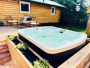 A hot tub in a wooden planter with a wooden deck and chairs in the background.