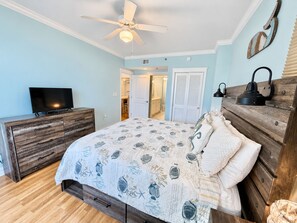 Ein Schlafzimmer mit Bett, Schminktisch, Fernseher, Deckenventilator und einer Tür zu einem Badezimmer.
